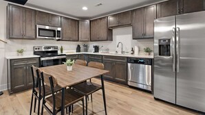 A modern kitchen with dark wood cabinets, stainless steel appliances, and a wooden dining table with chairs. - NEW ~ Charming, Cozy Apt DWTN Murfreesboro, TN (Murfreesboro)