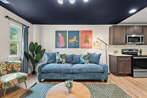 Una sala de estar con sofá, una mesa de comedor y una zona de cocina con armarios y electrodomésticos.