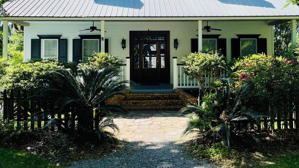 Uma casa de dois andares com telhado empena, varanda frontal e base de tijolos.