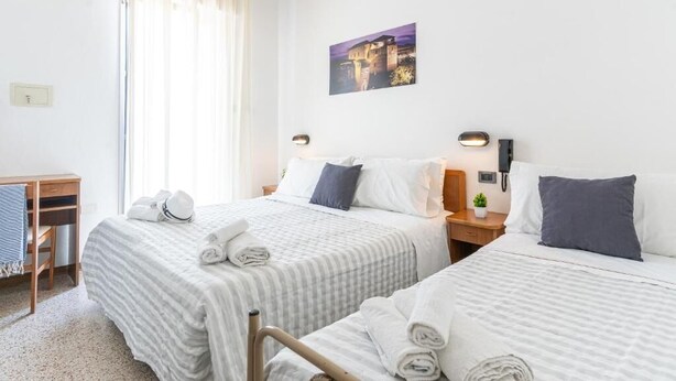A hotel room with two beds, a desk, a chair, a small plant, and a painting on the wall. - Hotel Lariana (Rimini)