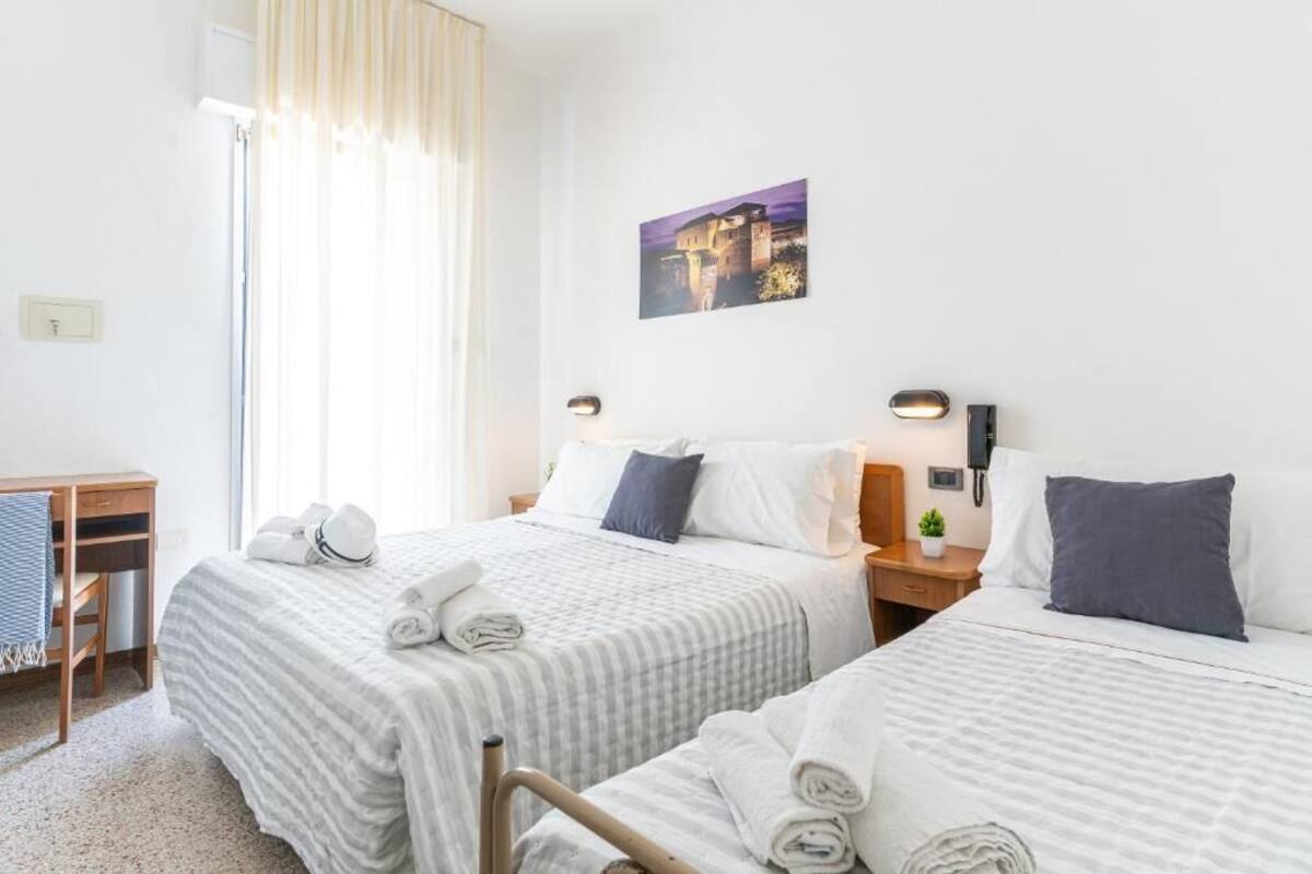 Ein Hotelzimmer mit zwei Betten, einem Schreibtisch, einem Stuhl, einer kleinen Pflanze und einem Bild an der Wand.