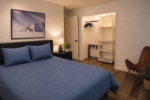 Ein Schlafzimmer mit Bett, Nachttisch, Lampe, Stuhl und einem Kleiderschrank mit Regalen.