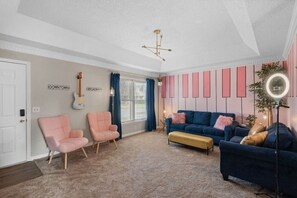 Un salon avec deux fauteuils roses, un canapé bleu, un petit banc, une guitare et un mur orné de panneaux verticaux.