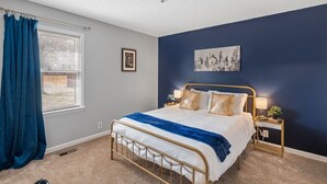 Una camera da letto con un letto, un comodino, una lampada, una finestra con tende e una luce a soffitto.