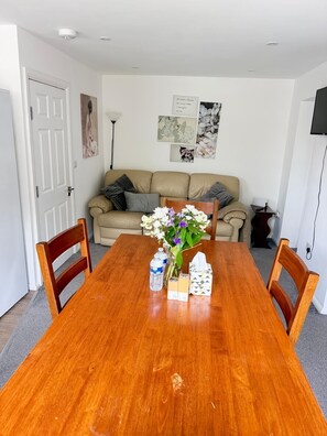 Un coin repas avec une table en bois, des chaises, un vase avec des fleurs, des bouteilles d’eau et une boîte de mouchoirs.