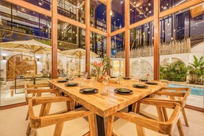 A dining area with a wooden table and chairs, surrounded by large windows and indoor plants. - Villa Nord, New 7 Bdr, Jacuzzi, Sauna, Ice bath (Kabupaten Badung)