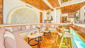 Un interior moderno con techo de madera, una amplia pared de piedra, una zona de estar con sofá y mesas, y una barra.