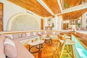 A modern interior with a wooden ceiling, a large stone wall, a seating area with a sofa and tables, and a bar area. - Villa Nord, New 7 Bdr, Jacuzzi, Sauna, Ice bath (Kabupaten Badung)