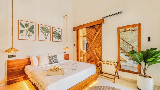 Un dormitorio con una cama de madera, un espejo grande y tres ilustraciones botánicas enmarcadas en la pared.