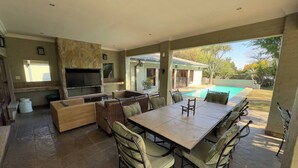 An outdoor patio with a dining table, chairs, a TV, and a pool. - Room-starling Room - Staynest Guesthouse (Johannesburg)