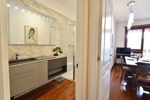 A modern bathroom with a marble wall, a sink, a mirror, and a shower. - An elegant apartment for up to 4 people, recently renovated with high-quality finishes, including parquet floors throughout. Located in the quaint Vanchiglietta neighborhood, it enjoys an ideal location: just 100 meters from the Lungo Po, perfect for str (Torino)