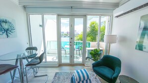 En moderne stue med en glasdør, der fører ud til en balkon, et spisebord med stole, en sofa og en lampe.