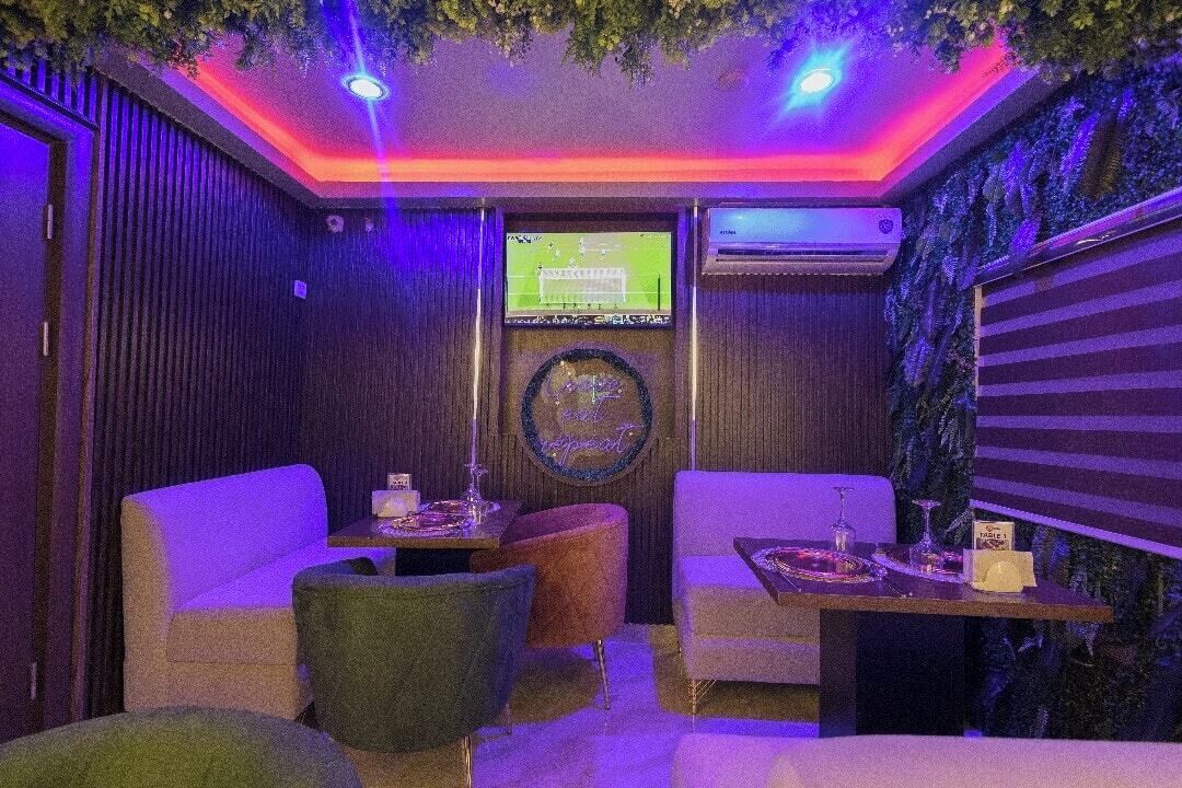 Una habitación con televisor, dos sofás, una mesa con bebidas y un aire acondicionado instalado en la pared.