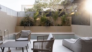 Um pátio moderno ao ar livre com mobiliário de vime, piscina e vegetação exuberante.