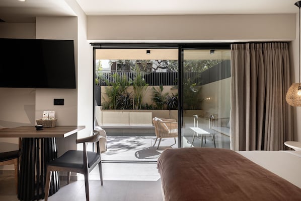 A modern hotel room with a large bed, a dining area, a TV, and a balcony with plants. - Executive Suite with Private pool by MonCasa (Agios Nikolaos)
