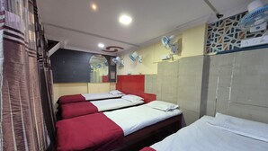 Habitación de hotel con cuatro camas, cada una con ropa de cama roja y blanca, un espejo grande y varios ventiladores de pared.