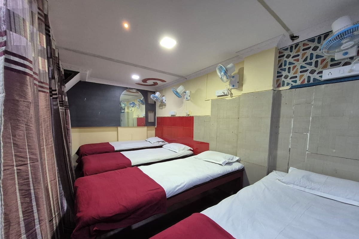 Habitación de hotel con cuatro camas, cada una con ropa de cama roja y blanca, un espejo grande y varios ventiladores de pared.