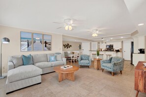 Ein Wohnzimmer mit einer Couch, Sesseln, einem Couchtisch und einem Essbereich mit einer Küche im Hintergrund.