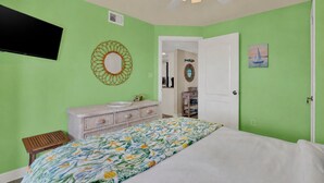 Une chambre à coucher avec un lit, une commode, un miroir et un ventilateur de plafond.