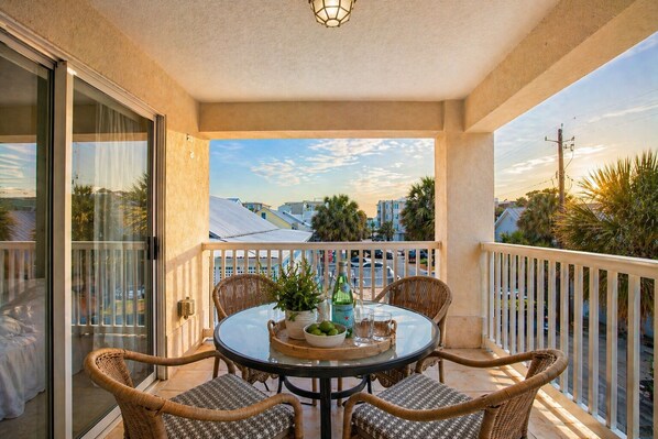 En balkong med en glasdörr, flätade stolar, ett runt bord och en flaska sprit.