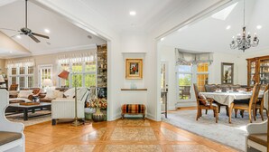 Een ruime woonkamer met een open haard, een eethoek met een kroonluchter en uitzicht op de omgeving.