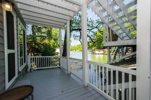 A covered deck with white railings, a table, and a view of a water body with boats.