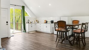 Een moderne keuken met witte kasten, een eettafel met vier stoelen en uitzicht op het landschap door grote ramen.