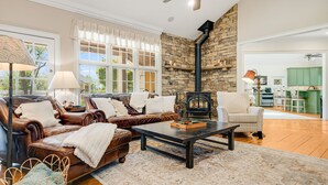 A living room with leather sofas, a coffee table, a stone wall, and a fireplace. - Luxury Estate w/ Pool, Hot Tub  Free Tix Sleeps 12 (Fletcher)
