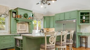 A kitchen with green cabinetry, a central island with bar stools, a refrigerator, and a window with a view. - Luxury Estate w/ Pool, Hot Tub  Free Tix Sleeps 12 (Fletcher)