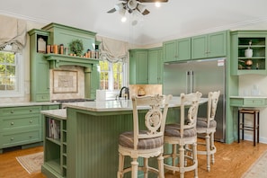 A kitchen with green cabinetry, a central island with bar stools, a refrigerator, and a window with a view. - Luxury Estate w/ Pool, Hot Tub  Free Tix Sleeps 12 (Fletcher)