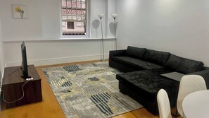 A modern living room with a black sofa, a flat-screen TV on a wooden stand, a patterned rug, and a window with a view of a building. - Cape Town Inner City Stay (Cape Town)
