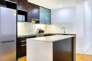 A modern kitchen with dark wood cabinets, a stainless steel refrigerator, a built-in oven, a microwave, and a large island with a sink. - Cape Town Inner City Stay (Cape Town)
