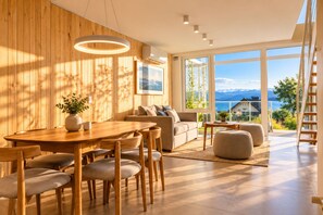 A modern interior with a wooden dining area, a sofa, and a view of the outdoors. - Signature Lake View · Luxury Residences B08 (San Carlos de Bariloche)
