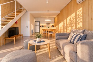 A modern living room with a sofa, a coffee table, a TV, and a staircase. - Signature Lake View · Luxury Residences B08 (San Carlos de Bariloche)