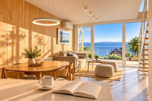 A modern living room with a wooden wall, a round dining table, and a sofa. - Signature Lake View · Luxury Residences B08 (San Carlos de Bariloche)