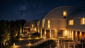 Un edificio moderno con tetto curvo, una scalinata centrale e un'area esterna ben illuminata di notte.
