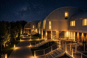 Un edificio moderno con techo curvo, una escalera central e iluminación exterior brillante en la noche.