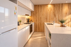 Eine moderne Küche mit weißen Schränken, einer Holzwand als Akzent und einem integrierten Backofen sowie einem Edelstahl-Spülbecken.