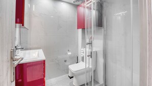 Ein modernes Badezimmer mit einer Duschkabine aus Glas, einer weißen Toilette und einem roten Schrank.