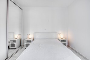 A minimalist bedroom with a large mirror, a bed with a white headboard, and bedside tables with lamps.