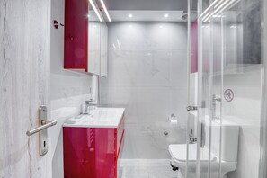 A modern bathroom with a glass shower enclosure, a white sink, and a red vanity.