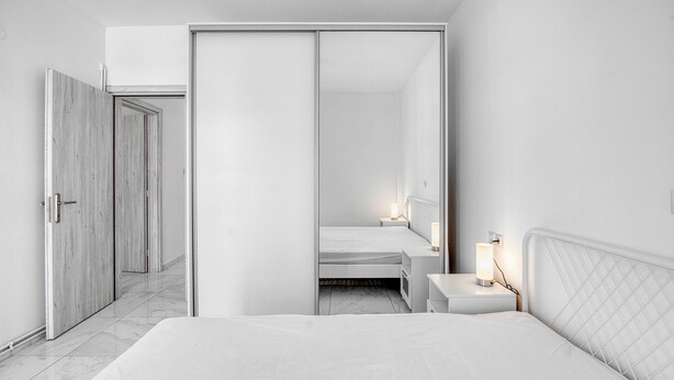 Ein modernes Schlafzimmer mit einem großen Bett, Nachttischen, einem Kleiderschrank und einem Beistelltisch mit Lampe.