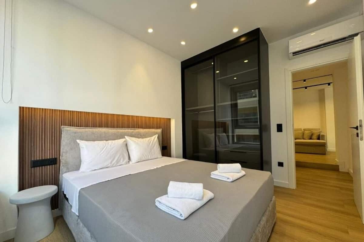 A modern hotel room with a large bed, a bedside table, a built-in wardrobe, and a separate seating area.