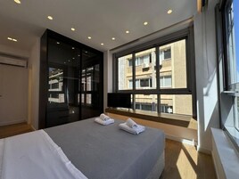 Habitación de hotel moderna con una cama grande, televisión, ventana con vista a edificios y armario con puerta corredera.