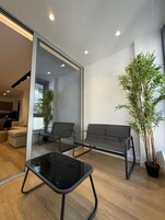 Una sala de estar moderna con un separador de vidrio, una mesa de centro negra, dos sillas negras, un sofá gris y una planta en maceta.