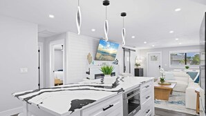 Une cuisine moderne dotée d’un îlot en marbre, de luminaires suspendus et d’une grande fenêtre.
