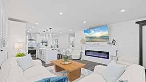 Un salon moderne avec une cheminée, des meubles blancs et une cuisine en arrière-plan.
