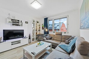 A modern living room with a flat-screen TV, a sofa, a coffee table, and a bookshelf. - Big one Bedroom Apartment near Airport & City Center (Schwechat)