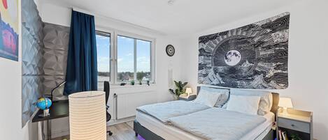A modern bedroom with a bed, a large window, a wall tapestry, and a globe on a desk.
