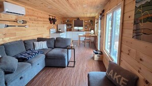 A cabin interior with a wooden ceiling, a sofa, a dining table, and a kitchen area.